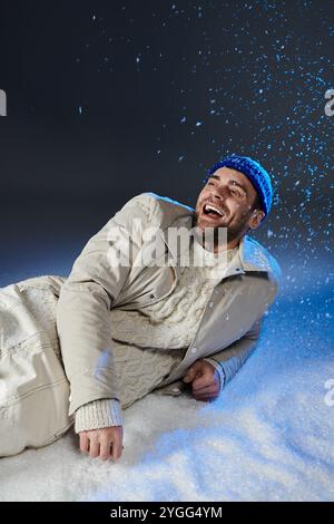 Ein junger Mann, warm gekleidet, lächelt hell, während Schneeflocken im Winter um ihn herum tanzen. Stockfoto