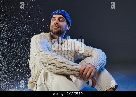 Der gutaussehende junge Mann sitzt bequem und genießt eine magische Atmosphäre aus schwebenden Schneeflocken. Stockfoto