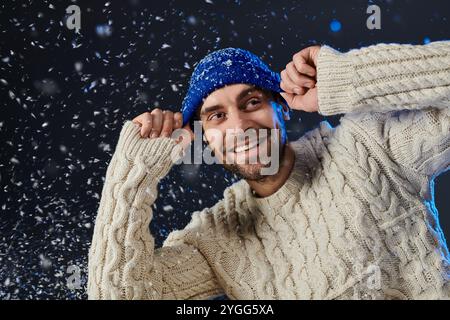 Ein junger Mann, warm gekleidet, lächelt, während Schneeflocken in einem Winterwunderland um ihn fallen. Stockfoto