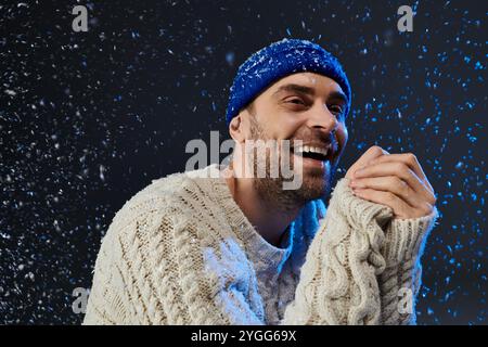 Ein junger Mann lächelt breit, umgeben von fallenden Schneeflocken, strahlt Wärme und Glück aus. Stockfoto