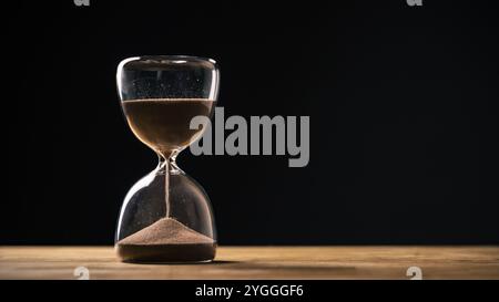 Sandglas auf schwarzem Hintergrund, fließende goldene Sandkörner, die auf einen Haufen fallen, Nahaufnahme. Veränderungs-, Instabilität- und Transienzkonzepte. Stockfoto