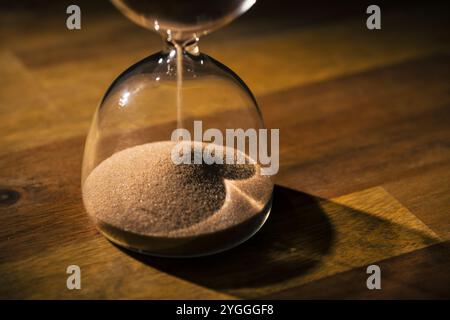 Sandglas auf schwarzem Hintergrund, fließende goldene Sandkörner, die auf einen Haufen fallen, Nahaufnahme. Veränderungs-, Instabilität- und Transienzkonzepte. Stockfoto