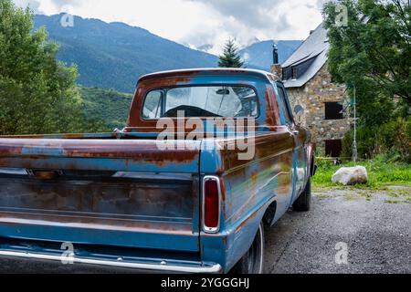 Ein original amerikanischer benzinbetriebener Pickup-Van, der komplett mit lackiertem Rost restauriert wurde, parkt im Garten eines Landhauses aus Stein mit einem schwarzen Stockfoto