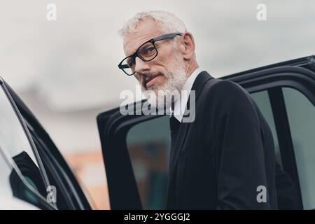 Selbstbewusster Geschäftsmann, der in formellem Anzug aus dem Auto steigt, auf der Stadtstraße in einem urbanen Ambiente. Stockfoto