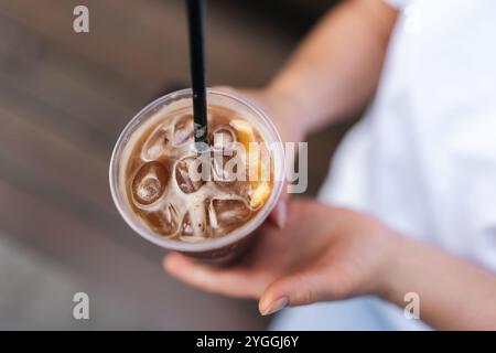 Nahaufnahme von oben auf die weibliche Hand, die Eisgetränk hält, Eiskaffee auf der Stadtstraße. Frau trinkt kalten Sprudeltee durch Stroh, Stockfoto