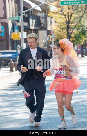 Ein Paar, das den New York Marathon 2024 in Kostümen und Handys in der Hand hat. An der Bedford Ave in Williamsburg um die 16-km-Marke. Stockfoto