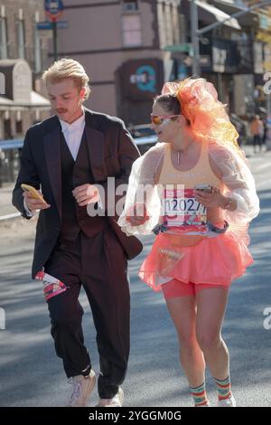 Ein Paar, das den New York Marathon 2024 in Kostümen und Handys in der Hand hat. An der Bedford Ave in Williamsburg um die 16-km-Marke. Stockfoto