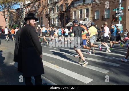 Ein orthodoxer jüdischer Mann denkt darüber nach, wie man die Straße überquert und dem Ansturm der Läufer beim New York Marathon 2024 ausweichen kann. In Williamsburg, Brooklyn Stockfoto