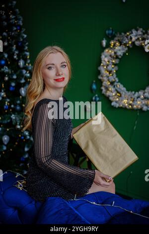 Glückliche junge Frau, die eine Geschenkbox neben dem weihnachtsbaum hält Stockfoto