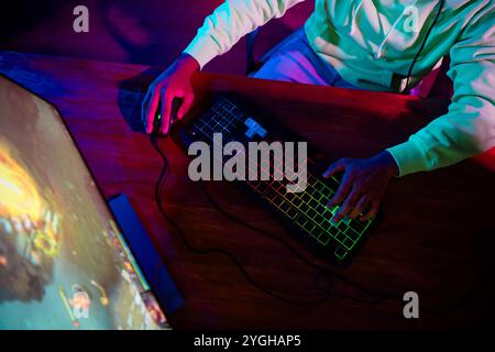 Zugeschnittenes Foto des Spielers junger männlicher Gebrauch Tastatur Maus Sitz Tisch Spiel Computerstrategie Spiel spät Nacht Raum Indoor lila blau Neonlicht Stockfoto