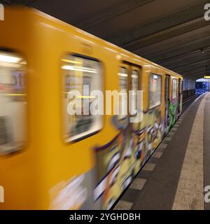 U-Bahn. Berlin. Kottbusser Tor. Durchfahrender Zug. gelber Wagen. gelber Zug. Graffiti. Gleis. Plattform. Tageslicht. Stahlträger. Geschwindigkeit. Vorbeifahrender Zug. Stockfoto