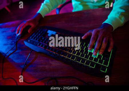Zugeschnittenes Foto von süßen jungen Mann verwenden Tastatur Maus sitzen Tisch Spiel Gamer Computer lila blau Neonlicht drinnen spät in der Nacht Stockfoto