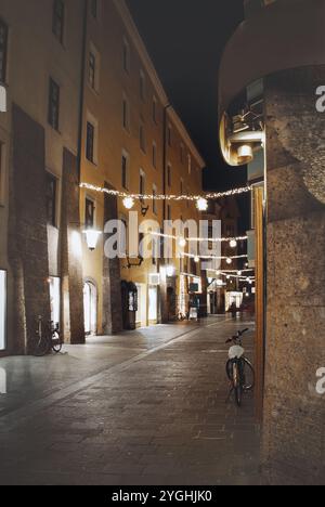 Mittelalterliche Gasse in Innsbruck Tirol Österreich. Straße bei Nacht mit einem Fahrrad, das an eine Wand gelehnt ist. Die Straße ist leer und die Lichter sind an Stockfoto