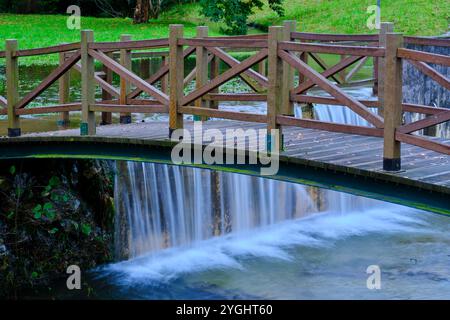 Nahaufnahme einer hölzernen Brücke über einen kleinen Wasserfall im Fluss Saja, in Cabezon de la Sal, Kantabrien. Spanien. Stockfoto