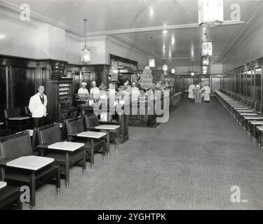 Werfen Sie einen Blick hinter die Kulissen des Chicago der 1920er Jahre mit diesem seltenen Einblick in den Speisesaal oder die Cafeteria des Drake Hotels. Dieses Vintage-Foto zeigt das klassische Art déco-Design, Marmorakzente und formelle Uniformen, die den Luxus-Hotelservice im frühen 20. Jahrhundert prägten. Perfekt für Geschichtsliebhaber, die sich für Vintage-Gastfreundschaft, Hotelbetrieb und die versteckte Eleganz ikonischer amerikanischer Hotels interessieren. Stockfoto