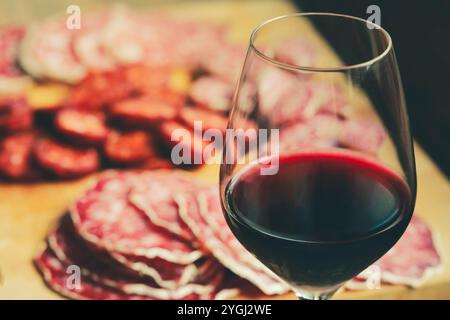 Selektiver Schwerpunkt auf einem Glas Rotwein mit traditioneller Salami, die auf Schneidebrett geschnitten wird Stockfoto