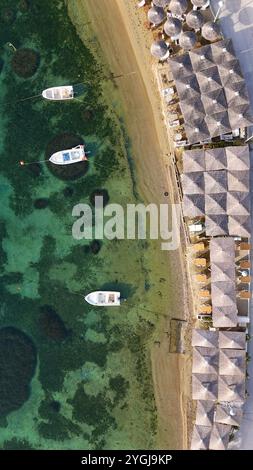 Blick aus der Vogelperspektive auf das luxuriöse Strandresort mit Strohbungalows, kristallklarem türkisfarbenem Wasser und vertäuten Booten Stockfoto