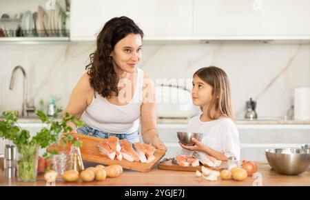 Glückliche Mutter und ihre Tochter bereiten Lachs zum Backen in der Küche vor Stockfoto