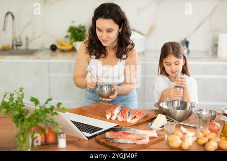 Glückliche Mutter und Tochter bereiten Lachs in der Küche vor Stockfoto