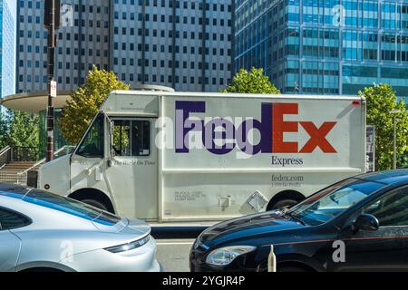 Ein Fedex-Truck fährt eine befahrene Straße entlang. Der Stapler ist weiß und hat ein violettes und orangefarbenes Logo an der Seite. Die Straße ist voll mit Autos, inklusive Stockfoto