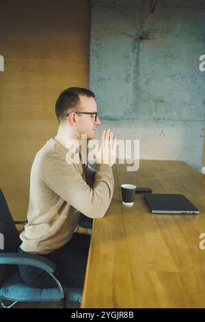 Seitenansicht eines männlichen Geschäftsmannes in legeren Kleidern, der sich Sorgen machte, ob er sich auf dem Tisch im Konferenzraum in einem modernen Büro niederlehnte Stockfoto