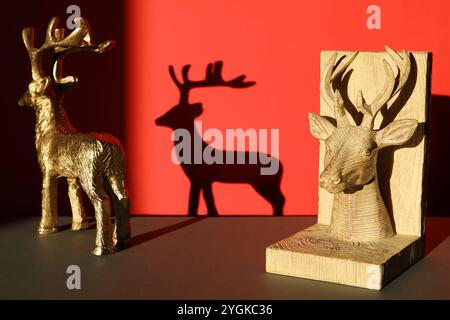 Dekorative Hirschfiguren auf schwarzem Tisch vor rotem Hintergrund mit Schatten Stockfoto