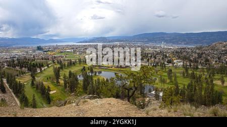 Ein breiter Panoramablick auf Kelowna, der die Skyline der Stadt, die umliegenden Golfplätze und den malerischen See vor einer bergigen Kulisse erfasst. Stockfoto