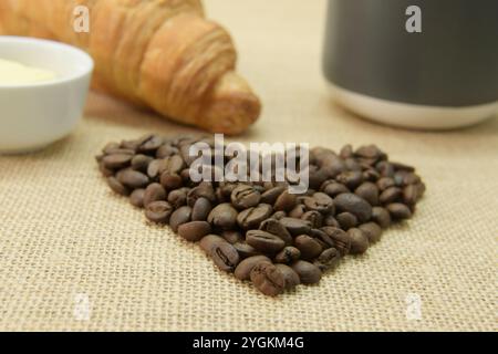 Frühstück Essen und Getränke Konzept, Kaffeebohnen in Herzform mit Croissant und Becher, Naturprodukt für den Hausgebrauch, Morgengetränk Stockfoto