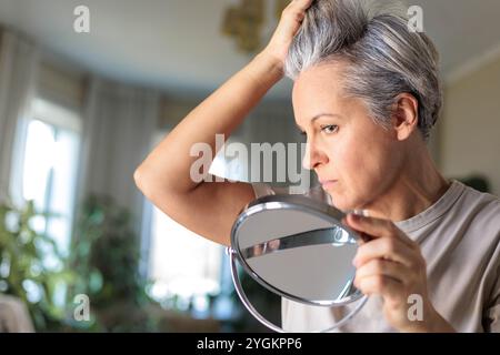 Grauhaarige, schockierte weiße Frau mittleren Alters schaut ihr graues Haar an Stockfoto
