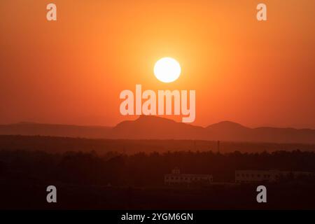 Die Sonne untergeht dramatisch hinter einer Bergkette und strahlt ein warmes Orange über die Silhouette der Landschaft. Stockfoto