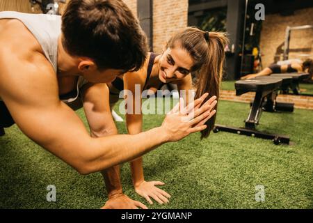 Ein Mann und eine Frau teilen sich während eines Workouts im Fitnessstudio einen motivierenden High-Five. Die Atmosphäre ist energiegeladen und betont die Teamarbeit. Stockfoto