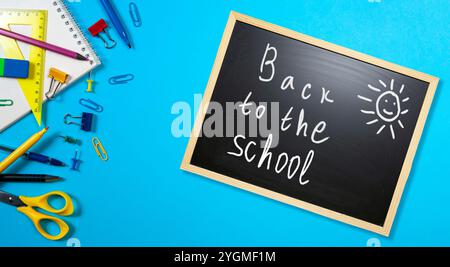 Farbenfrohe Schreibwaren umgeben eine Tafel, auf der der Satz zurück zur Schule vor einem hellblauen Hintergrund dargestellt wird. Stockfoto