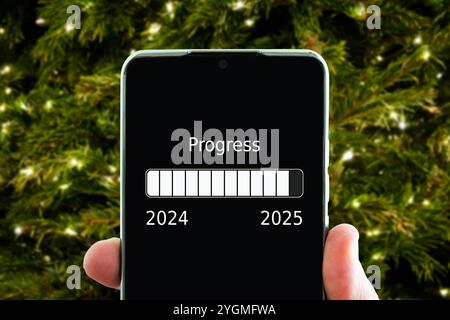 Das Konzept des Jahreswechsels von 2024 auf 2025. Smartphone auf der Computertastatur mit dem Ladevorgang des neuen Jahres. Ende 2023 Stockfoto