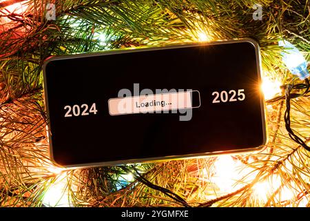 Das Konzept des Jahreswechsels von 2024 auf 2025. Smartphone auf der Computertastatur mit dem Ladevorgang des neuen Jahres. Ende 2023 Stockfoto