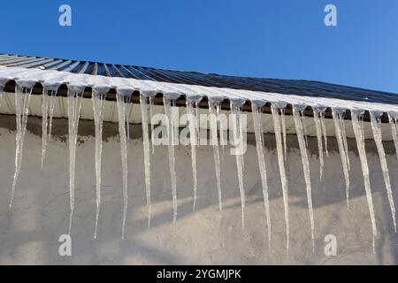 Scharfe Eiszapfen und geschmolzener Schnee hängen von Dachtrassen. Wunderschöne, transparente Eiszapfen, die langsam über ein Dach gleiten. Stockfoto