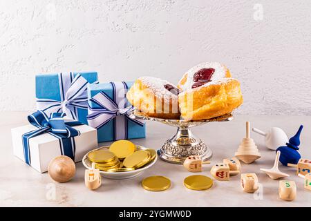 Viele Feiertagskästen, hölzerne Dreidels, Goldmünzen, Donuts in einer silbernen Vase vor einer grauen strukturierten Wand. Vorderansicht. Das Konzept von Hanukka Stockfoto