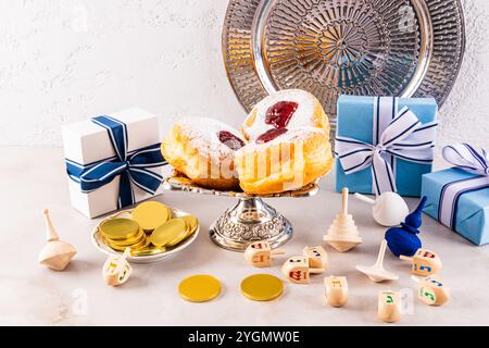 Ein wunderschöner Hintergrund für den jüdischen Feiertag von Hanukka. Frisch gebackene Donuts auf einem Silberteller, Silbertablett, Dreidels, Münzen, Geschenke. Vorderansicht Stockfoto