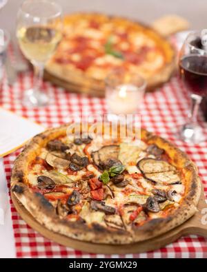 Köstliche italienische Pizza mit verschiedenen Belägen auf rotem kariertem Tischtuch in authentischem Ambiente Stockfoto