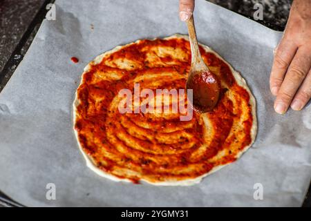 Person, die Tomatensauce zu Pizza auf Pergamentpapier hinzufügt Stockfoto