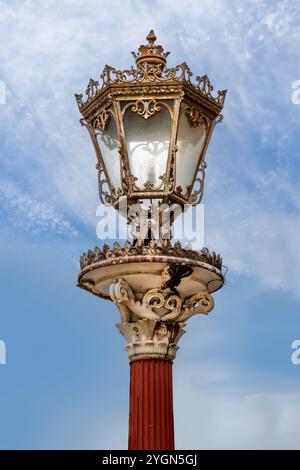 Alte Vintage Straßenlaterne mit goldenen dekorativen Elementen und einem roten Pfosten Stockfoto