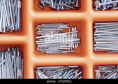 Sammlung von Nägeln, Daumennägeln, Schrauben, Kunststoff und Bolzen in Kunststoffkiste auf dem Holztisch Stockfoto