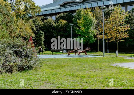 Ruhige Holzbank entlang des Weges eines Stadtparks. Ein Wald mit Reifen Laubbäumen und grünem Rasen macht es zu einem magischen Ort zum Ausruhen. Hochwertige Pho Stockfoto