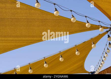 Markise-Textur des Stoffdachs aus Segeltuch mit Reihen hängender Glühbirnenlampen auf blauem Himmel Hintergrund. Stockfoto