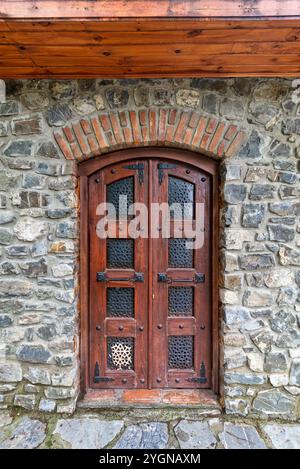 Die robuste Holztür ist mit aufwändigen Metallarbeiten versehen und bietet einen rustikalen Charme, eingerahmt von einer verwitterten Steinmauer in einer ruhigen ländlichen Umgebung Stockfoto