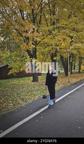 Eine ästhetische junge Frau mit schwarzem Mantel spaziert durch die bunten Baumallee im Herbstpark. Ruhige Herbstszene Stockfoto
