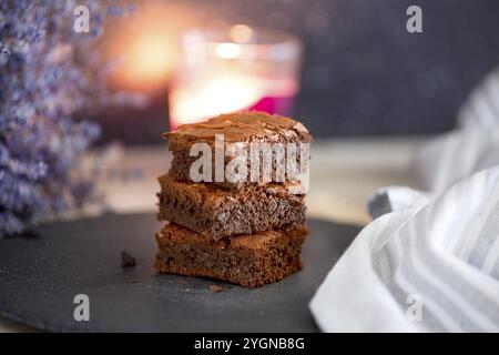 Hausgemachter Brownies-Kuchen mit dunkler Schokolade, gestapelt auf einer Steinplatte mit Kopierbereich. Lavendelblumen, Kerzenlicht Stockfoto