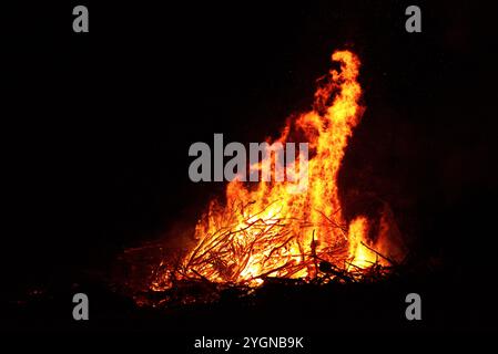 Großes Lagerfeuer mit Flammen, die nachts in der Luft schossen. Das Feuer hat die Farben Rot, Orange und Gelb. Da fliegen Funken in der Luft Stockfoto