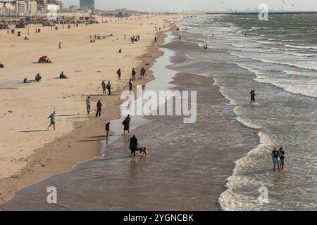 Menschen, die beim Sonnenuntergang am öffentlichen Strand in Scheveningen spazieren gehen. Kitesurfer segeln im Hintergrund. Den Haag, Niederlande - 10. Juli 2024: Menschen, die bei Sonnenuntergang am öffentlichen Strand in Scheveningen spazieren. Kitesurfer segeln im Hintergrund. Edit netherlands the hauge B97A7368 Stockfoto