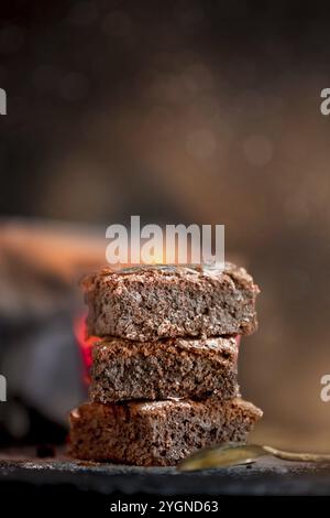 Hausgemachter Brownies-Kuchen aus dunkler Schokolade, gestapelt auf einer Steinplatte mit Kopierbereich, dunkler Hintergrund Stockfoto