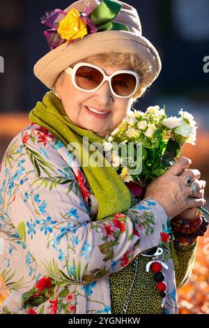 Porträt einer lächelnden achtzigjährigen Seniorin mit einem Blumenstrauß draußen an einem sonnigen Herbsttag Stockfoto